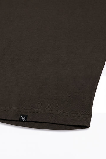 Close-up of a dark brown t-shirt hem showing a small black brand tag with a butterfly graphic on a white background.