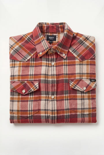 A folded long-sleeve plaid button-down shirt by Roxy, featuring a warm red, orange, beige, and brown tartan pattern with two chest pockets.